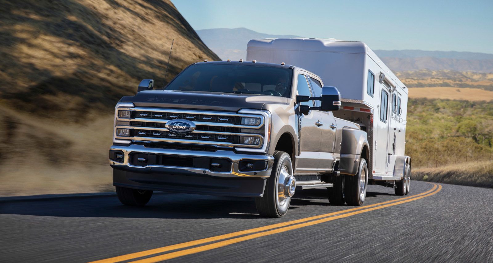 2026 Ford Super Duty F-350 - a brown 2026 Ford Super Duty F-350 towing a horse trailer on a winding road - Mayfield Ford - Ford new car dealership in Brampton, Ontario