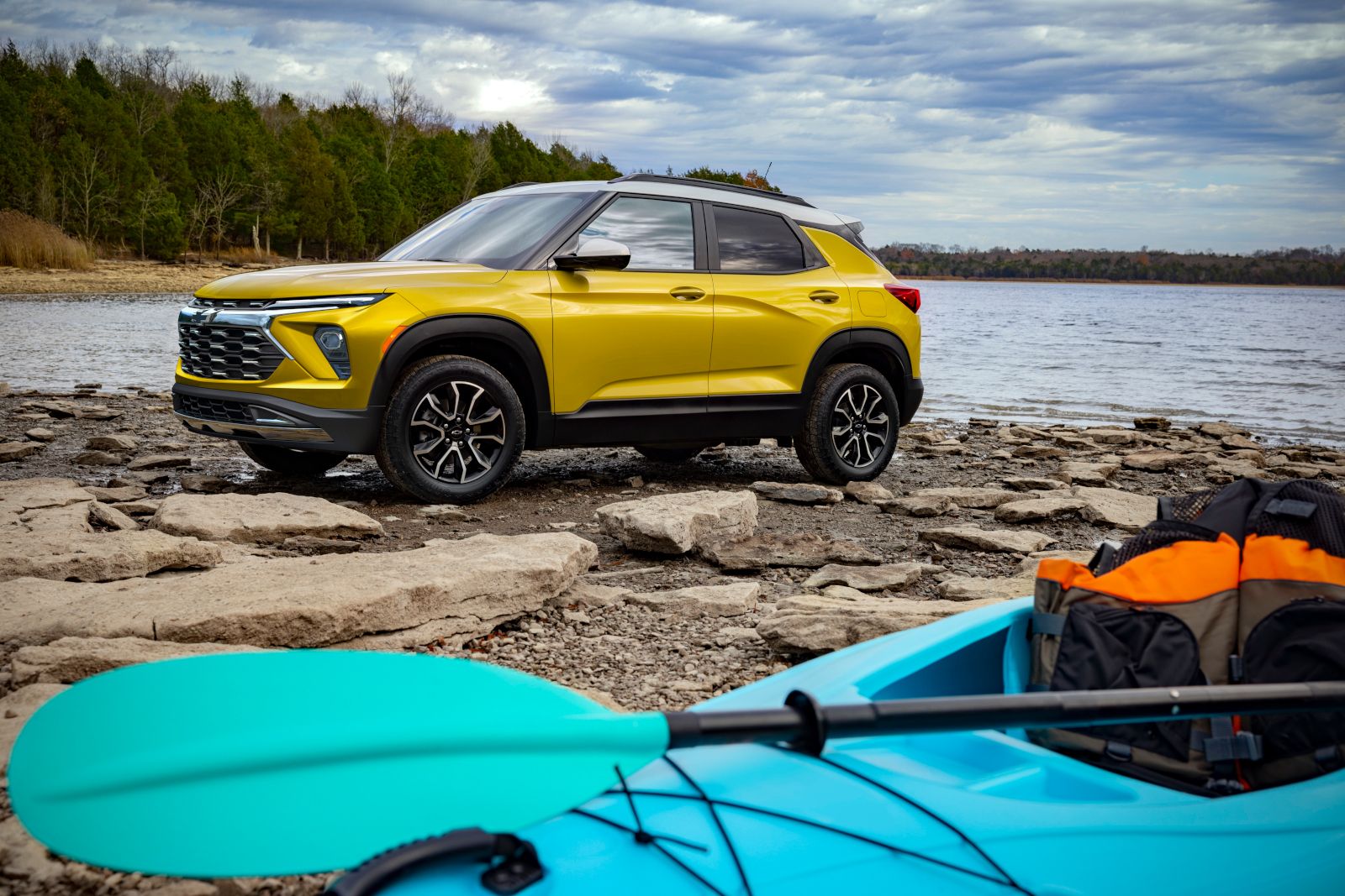 2026 Chevrolet Trailblazer - a yellow 2026 Chevrolet Trailblazer parked on a rocky shoreline by a lake with a kayak in the foreground - Applewood Chevrolet, Buick, GMC - New car dealership in Mississauga, Ontario