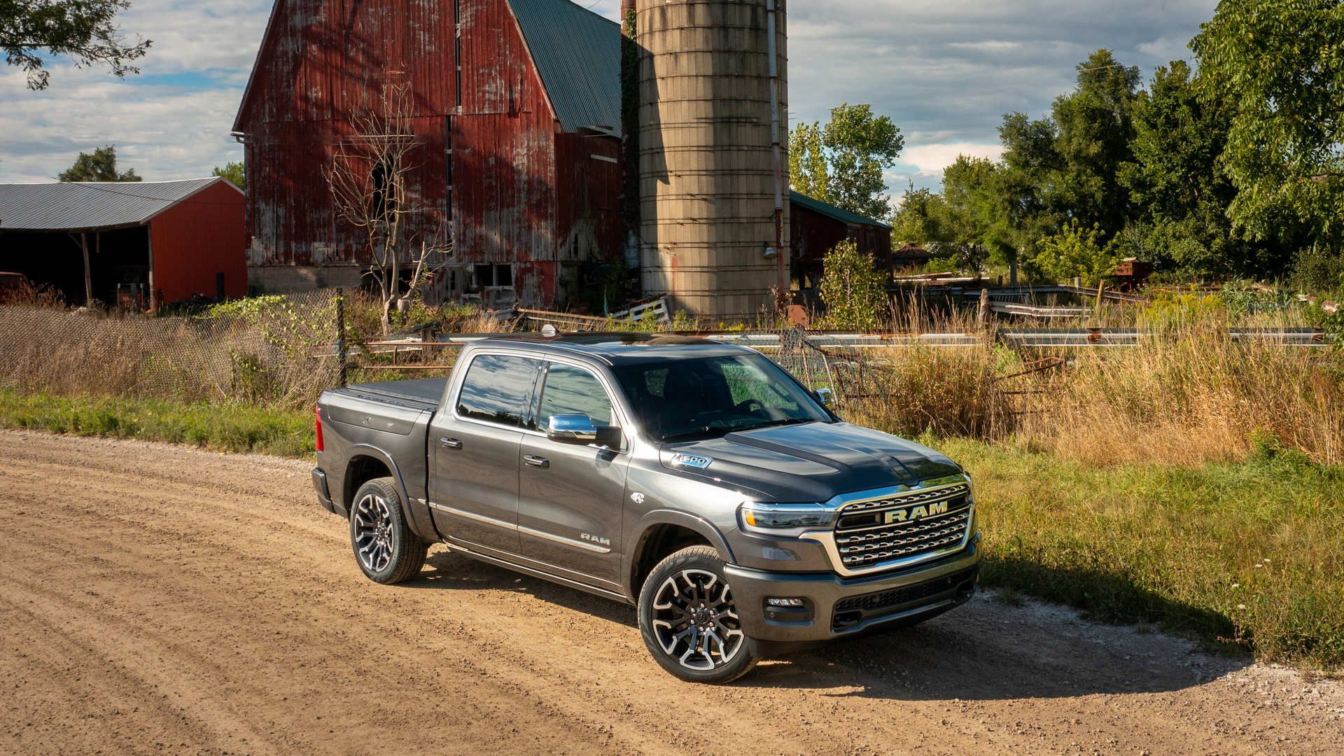 2026 RAM 1500 - front three-quarter view of a dark grey 2026 RAM 1500 pickup truck parked on a dirt road in front of a red barn - Humberview Group - New car dealerships in Ontario