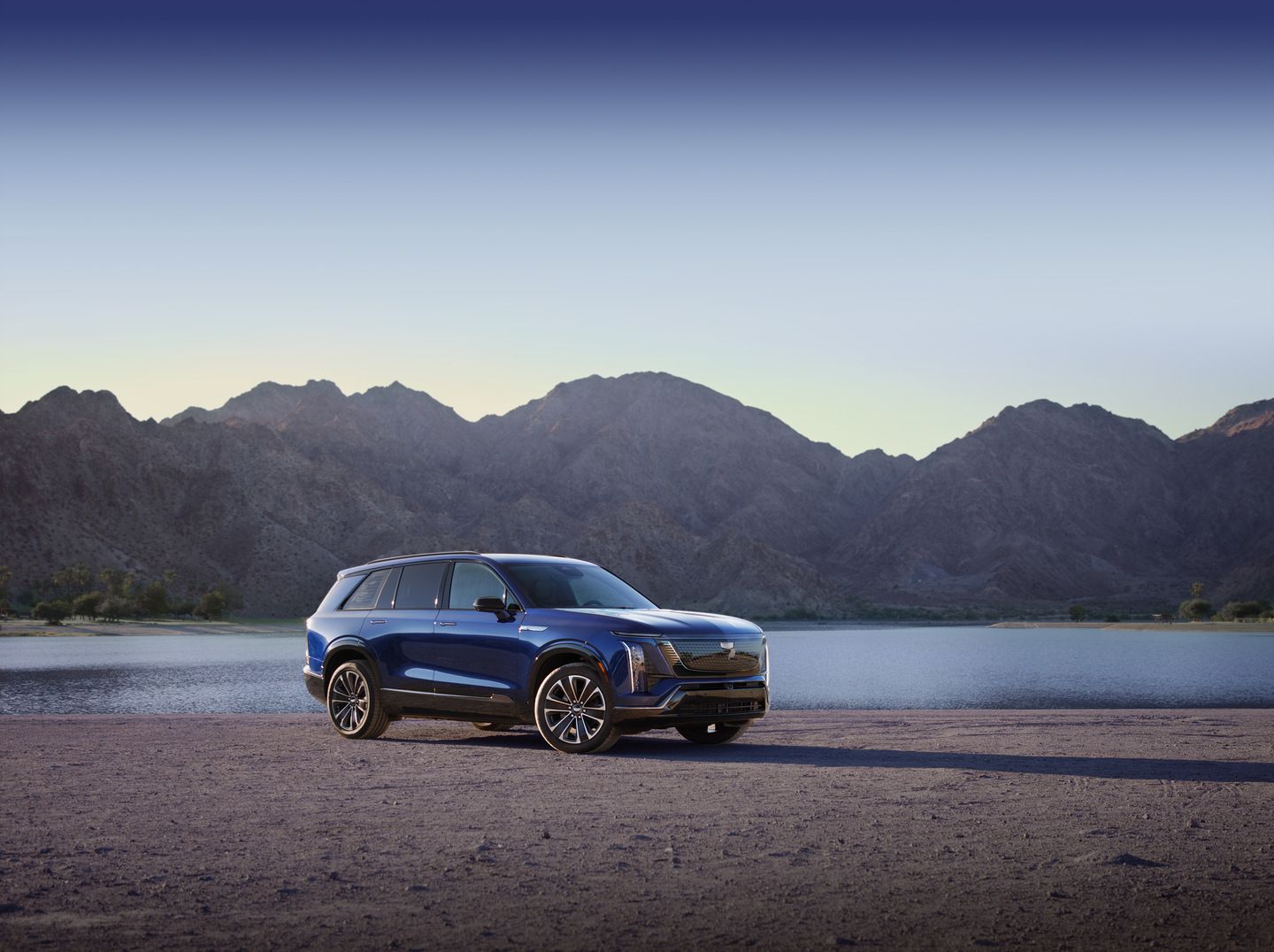 2026 Cadillac VISTIQ - front three-quarter view of a blue 2026 Cadillac VISTIQ parked in front of a lake and mountains - Applewood Cadillac - Cadillac new car dealership in Mississauga, Ontario