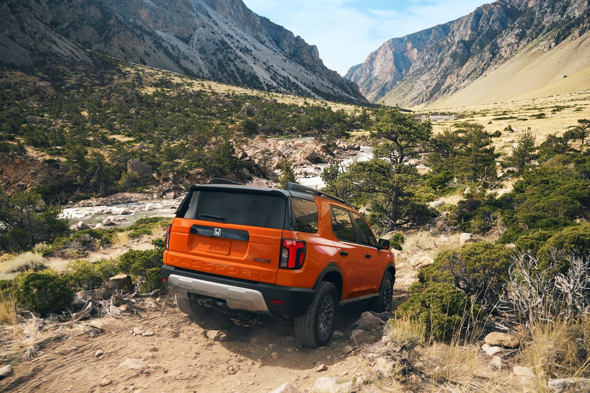 2026 Honda Passport - Rear angle view of an orange 2026 Honda Passport driving on a mountain dirt trail - Orangeville - Honda new car dealership in Orangeville, Ontario