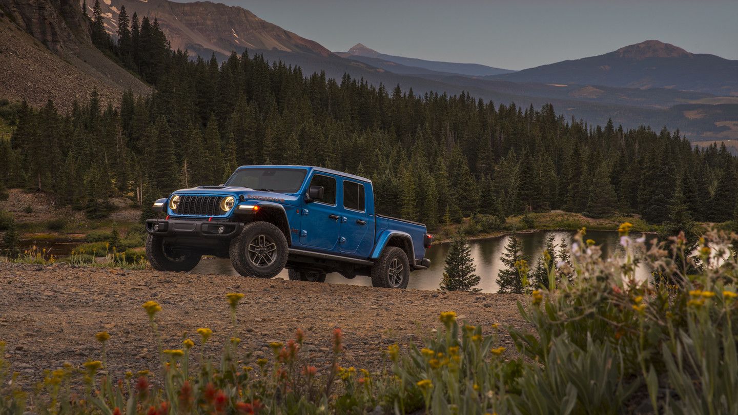 2026 Jeep Gladiator - A blue Jeep Gladiator pickup truck parked on a gravel path near a mountain lake at sunset - Cooksville Chrysler, Jeep, Dodge - New car dealership in Mississauga, Ontario