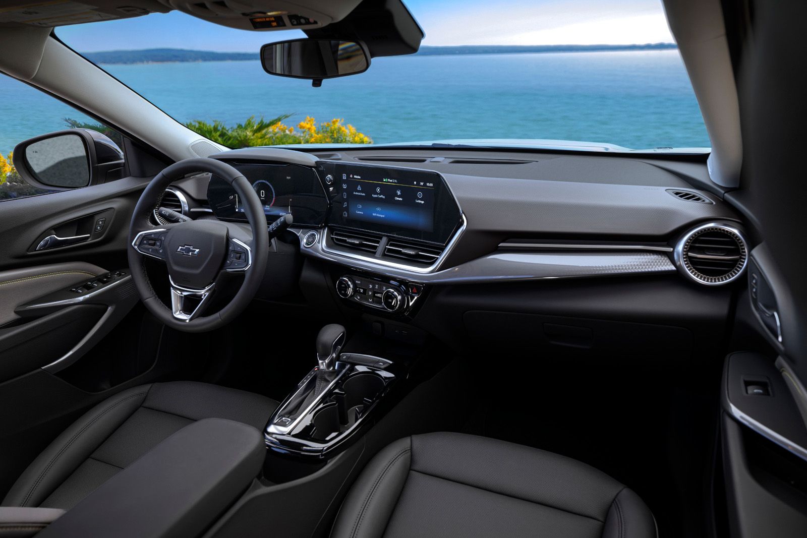 2026 Chevrolet Trax - View of the front cabin interior of a Chevrolet Trax featuring the dashboard, steering wheel, and infotainment screen with an ocean view through the windshield - Applewood Chevrolet, Buick, GMC - New car dealership in Mississauga, Ontario