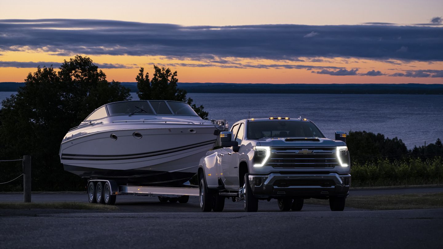 2026 Chevrolet Silverado 3500 HD - Low-angle front view of a white 2026 Chevrolet Silverado 3500 HD Dually towing a boat at dusk - Humberview Chevrolet, Buick, GMC - Chevrolet new car dealership in Toronto, Ontario