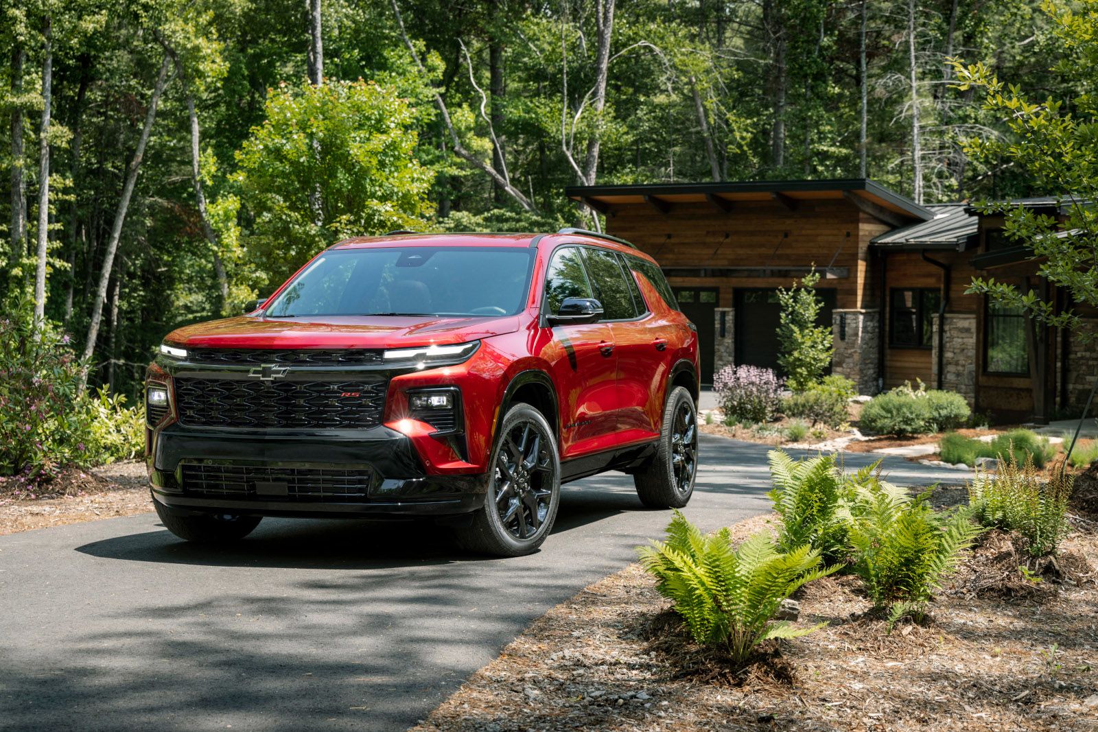 2026 Chevrolet Traverse - Front-quarter view of a red 2026 Chevrolet Traverse parked on a paved driveway in front of a modern wood-sided house - Humberview Chevrolet, Buick, GMC - Chevrolet car dealership in Toronto, Ontario
