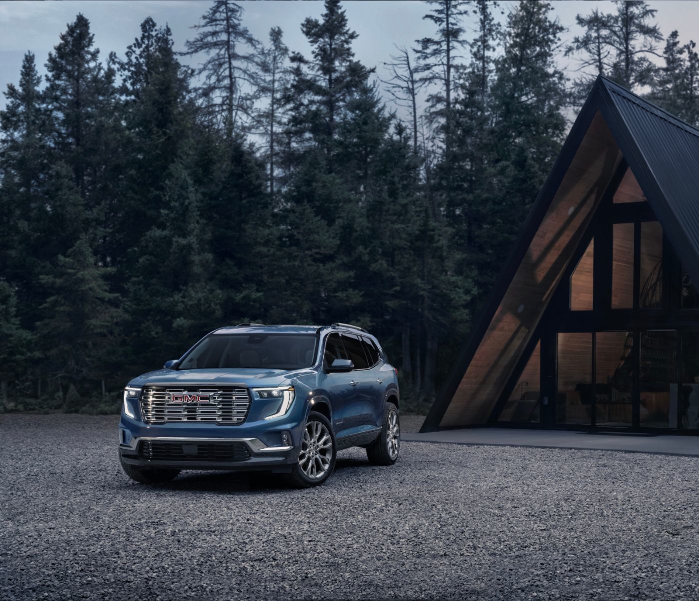 2026 GMC Acadia - Front-quarter view of a blue 2026 GMC Acadia parked on a gravel driveway next to a modern A-frame cabin - Humberview Chevrolet, Buick, GMC - GMC car dealership in Toronto, Ontario