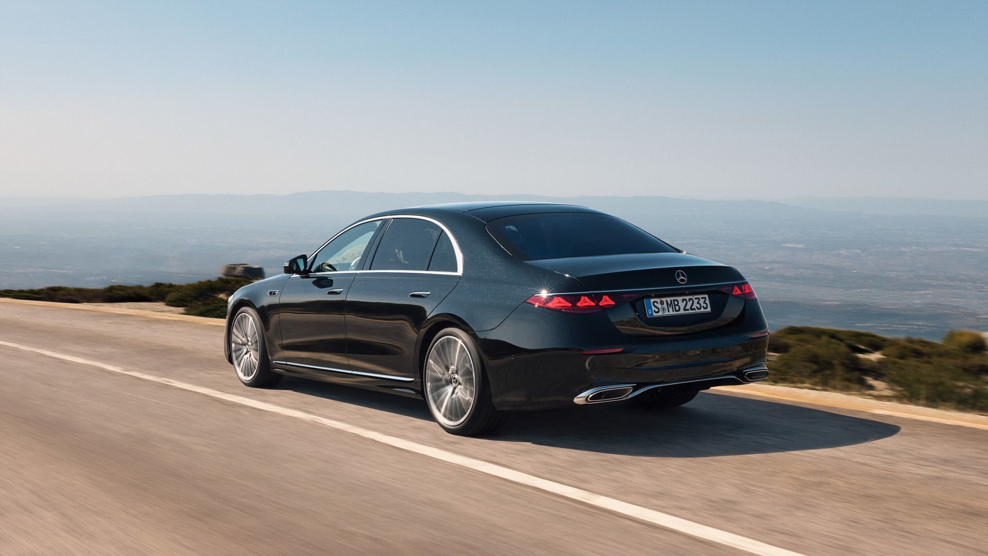 2027 Mercedes-Benz S-Class - rear three-quarter view of a black 2027 Mercedes-Benz S-Class sedan driving along a scenic mountain road - Humberview Group - New car dealerships in Ontario