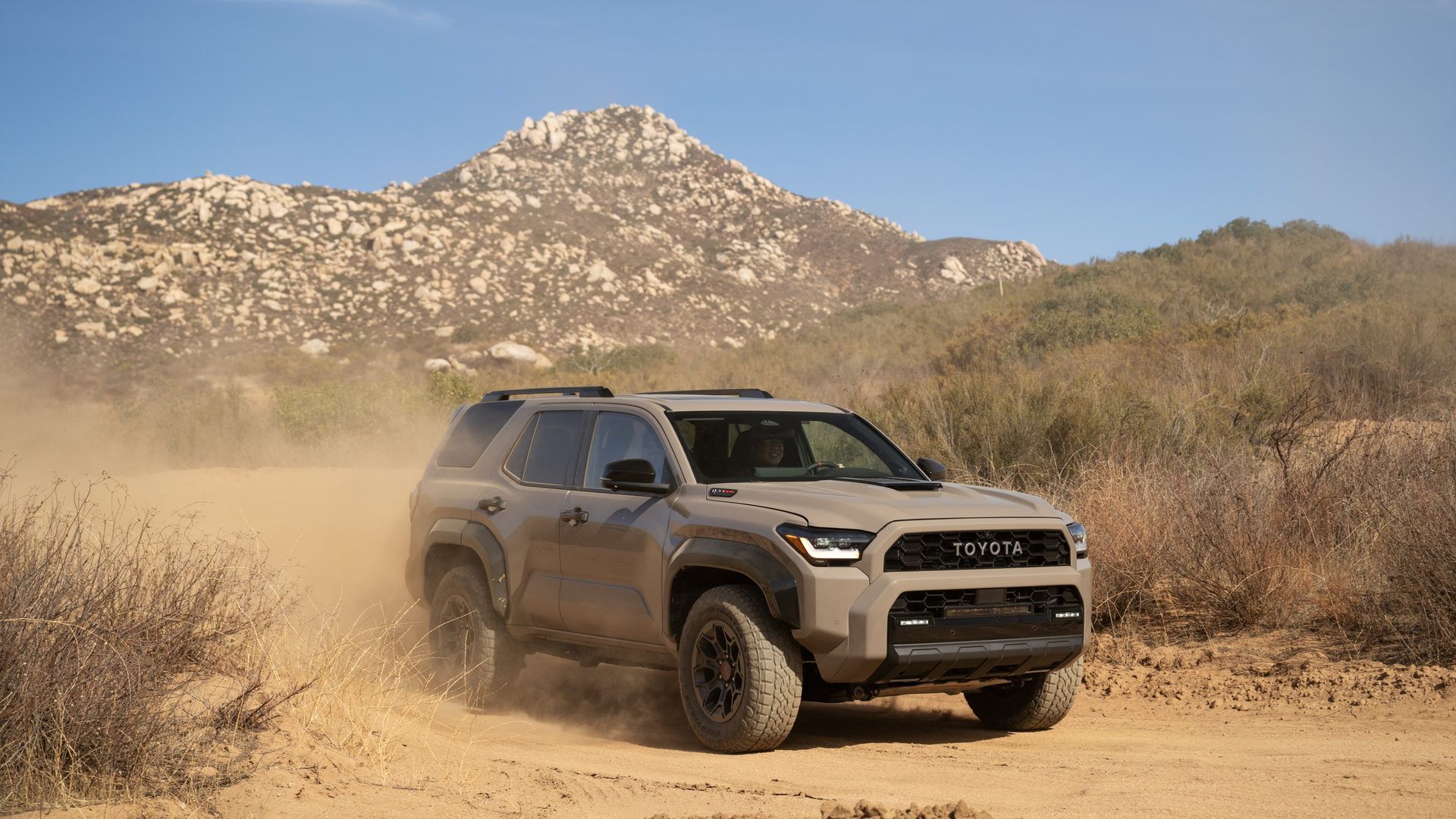 2026 Toyota 4Runner - A tan 2026 Toyota 4Runner TRD Pro driving off-road on a dusty trail with mountains in the background - Orangeville Toyota - Toyota new car dealership in Orangeville, Ontario