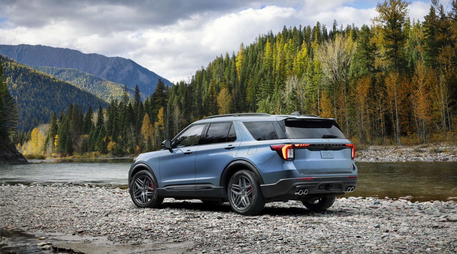 2027 Ford Explorer - rear three-quarter view of a blue 2027 Ford Explorer ST parked on a rocky riverbed - Bayfield Ford - Ford new car dealership in Barrie, Ontario