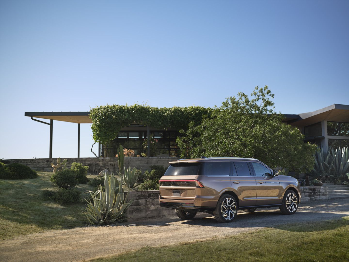 2026 Lincoln Navigator - a three-quarter rear view of a 2026 Lincoln Navigator in a rose gold colour driving on a driveway in front of a modern home - Bayfield Lincoln - Lincoln car dealership in Barrie, Ontario