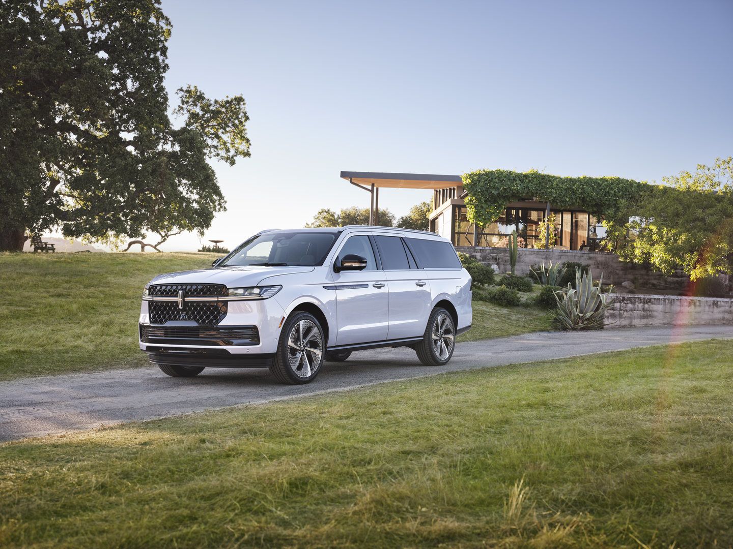 2026 Lincoln Navigator - a white 2026 Lincoln Navigator is shown in a three-quarter front view on a gravel driveway in a rural setting - Bayfield Lincoln - Lincoln car dealership in Barrie, Ontario