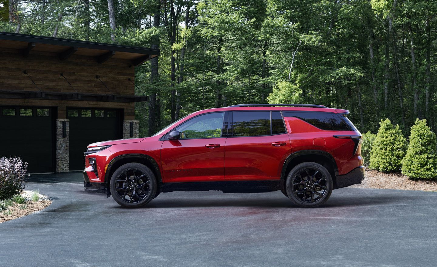 2027 Chevrolet Traverse - side profile view of a red 2027 Chevrolet Traverse RS parked in a driveway in front of a modern house - City Chevrolet, Buick, GMC - New car dealership in Toronto, Ontario