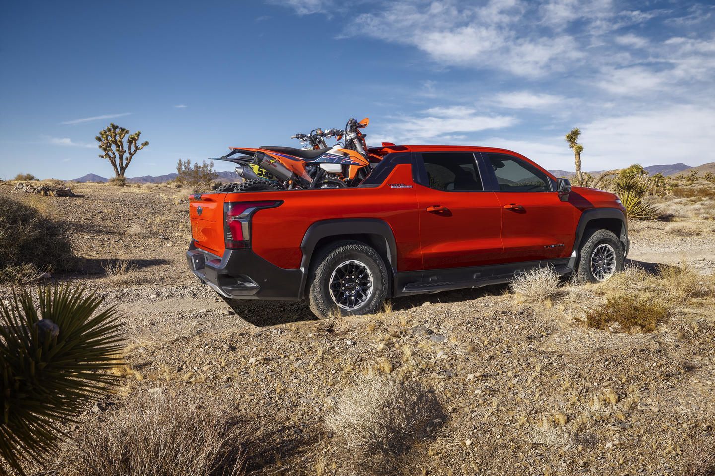 2026 Chevrolet Silverado EV - profile view of an orange 2026 Chevrolet Silverado EV Trail Boss carrying dirt bikes in the bed on a desert trail - Humberview Chevrolet, Buick, GMC - Chevrolet new car dealership in Toronto, Ontario