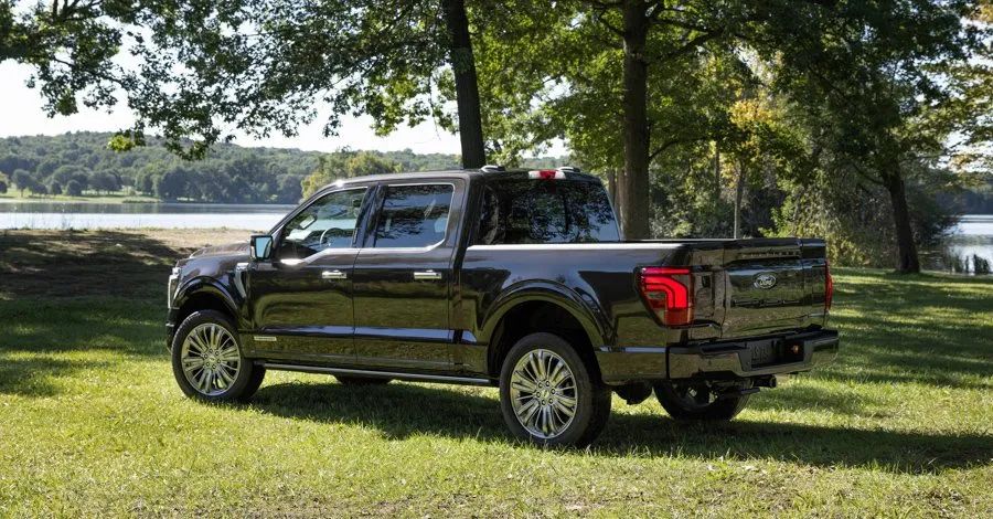 2027 Ford F-150 - rear three-quarter view of a dark 2027 Ford F-150 parked in a grassy area next to a lake - Mayfield Ford - New car dealership in Brampton, Ontario