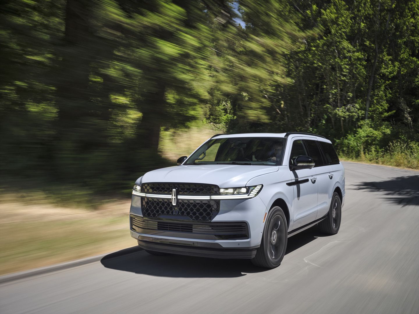 2027 Lincoln Navigator - front three-quarter view of a light blue 2027 Lincoln Navigator driving along a tree-lined road - Mayfield Lincoln - Lincoln new car dealership in Brampton, Ontario