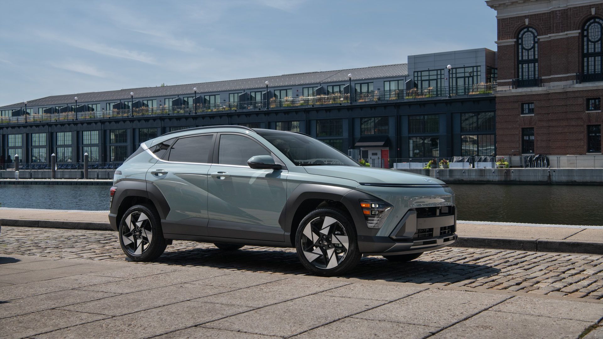 2027 Hyundai Kona - front three-quarter view of a sage green 2027 Hyundai Kona parked near a waterfront promenade - Woodstock Hyundai - Hyundai new car dealership in Woodstock, Ontario