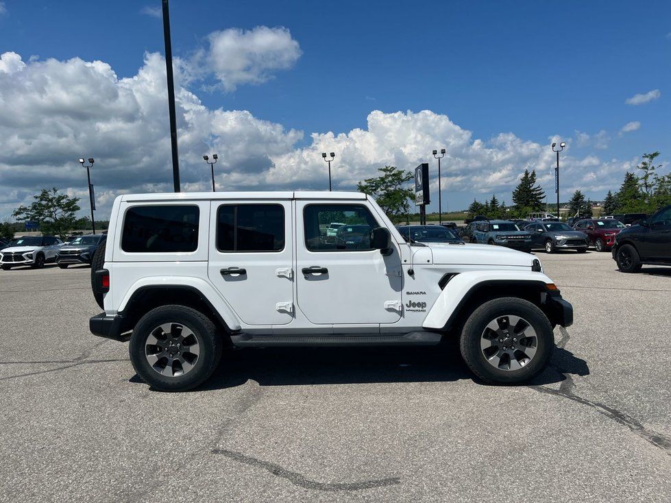 Jeep Wrangler - Side profile view of a white 4-door Jeep Wrangler Unlimited Sahara parked outside - AutoPark Barrie - Used car dealership in Barrie, Ontario