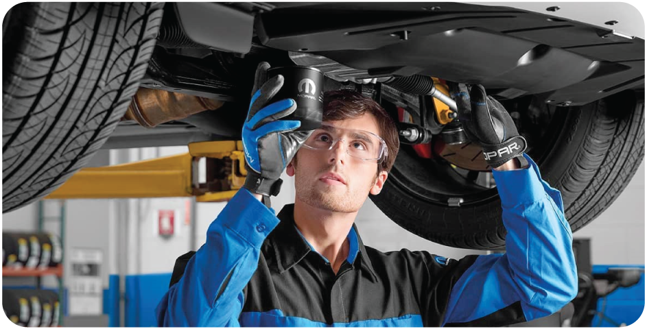 Chrysler Grand Caravan - a mechanic in a blue and black uniform wearing safety glasses and gloves replacing an oil filter under a car - Humberview Mobility - Accessible car dealership in Toronto, Ontario