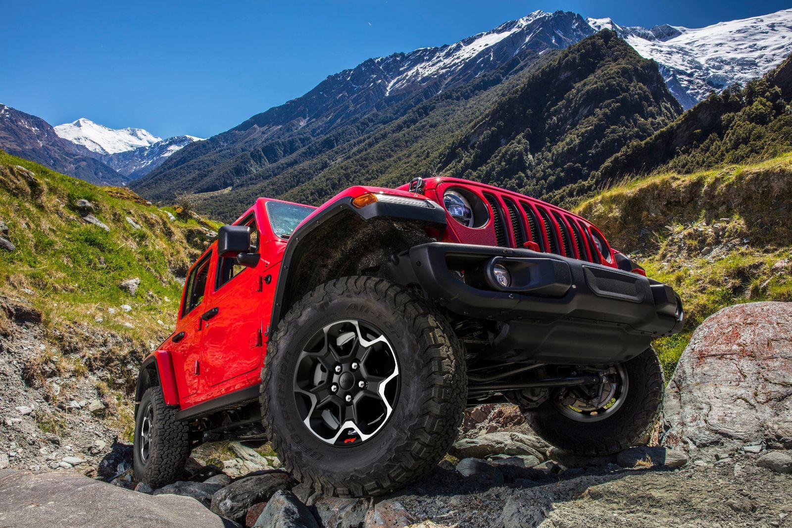 2027 Jeep Wrangler - front three-quarter view of a red 2027 Jeep Wrangler driving over rocks on a mountain trail - Cooksville Chrysler, Jeep, Dodge, Ram - Jeep car dealership in Mississauga, Ontario