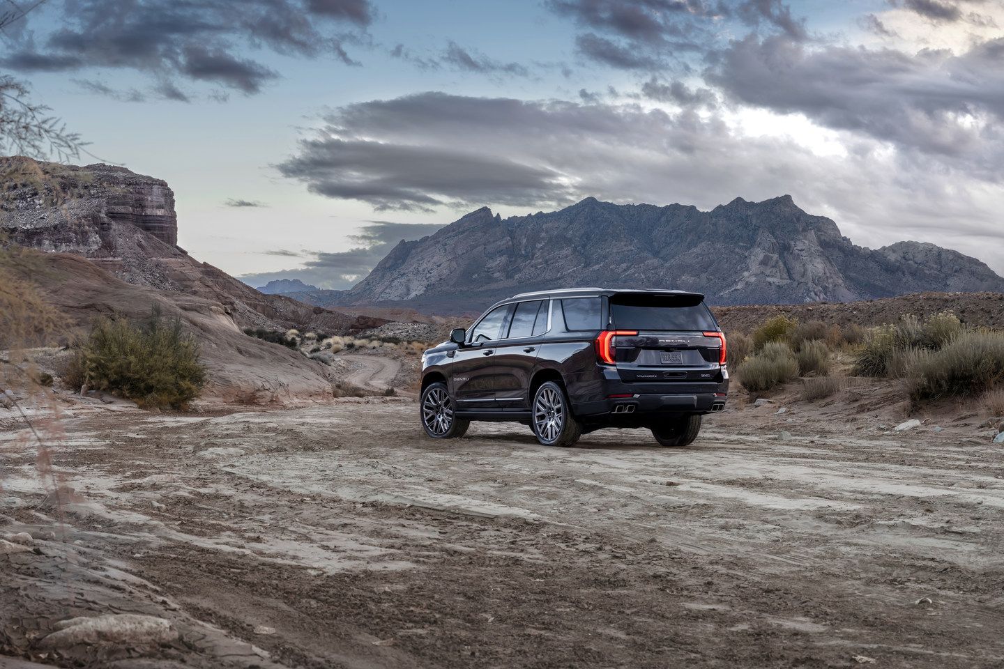 2027 GMC Yukon - rear three-quarter view of a dark 2027 GMC Yukon Denali parked on a dirt trail with mountains in the background - City Chevrolet, Buick, GMC - GMC new car dealership in Toronto, Ontario