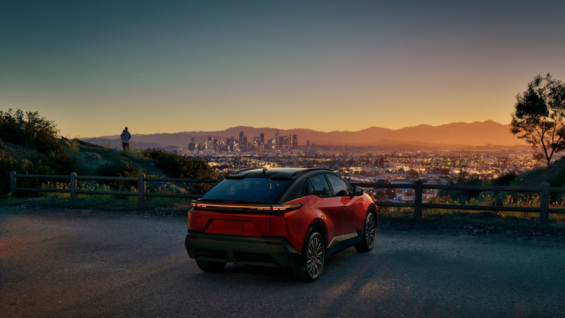 2027 Toyota C-HR - Rear view of a two-tone orange and black Toyota C-HR overlooking a city skyline at dusk - Georgetown Toyota - Toyota new car dealership in Georgetown, Ontario