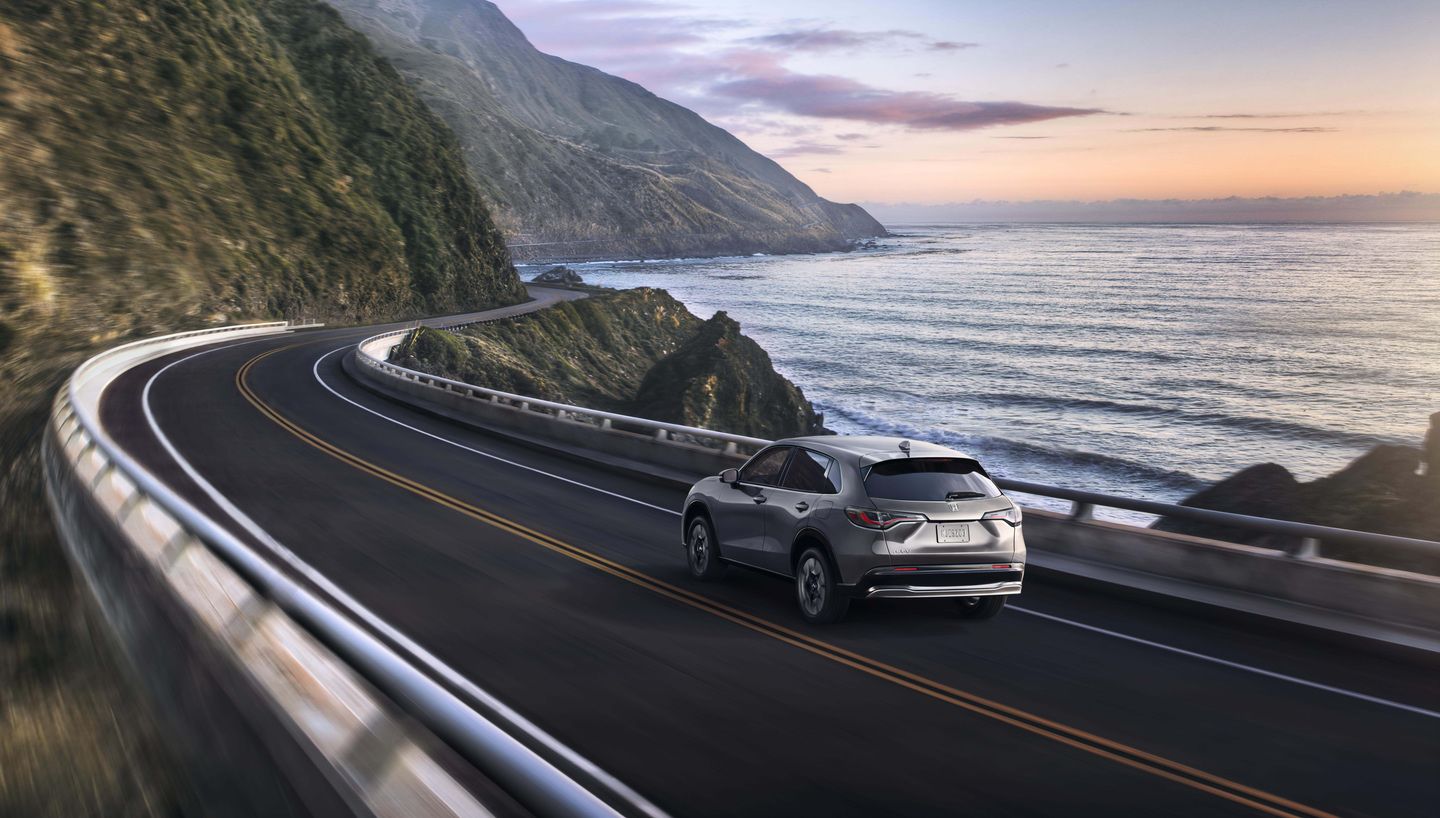 2027 Honda HR-V - rear three-quarter view of a silver 2027 Honda HR-V driving along a winding coastal highway at dusk - Goderich Honda - Honda car dealership in Goderich, Ontario
