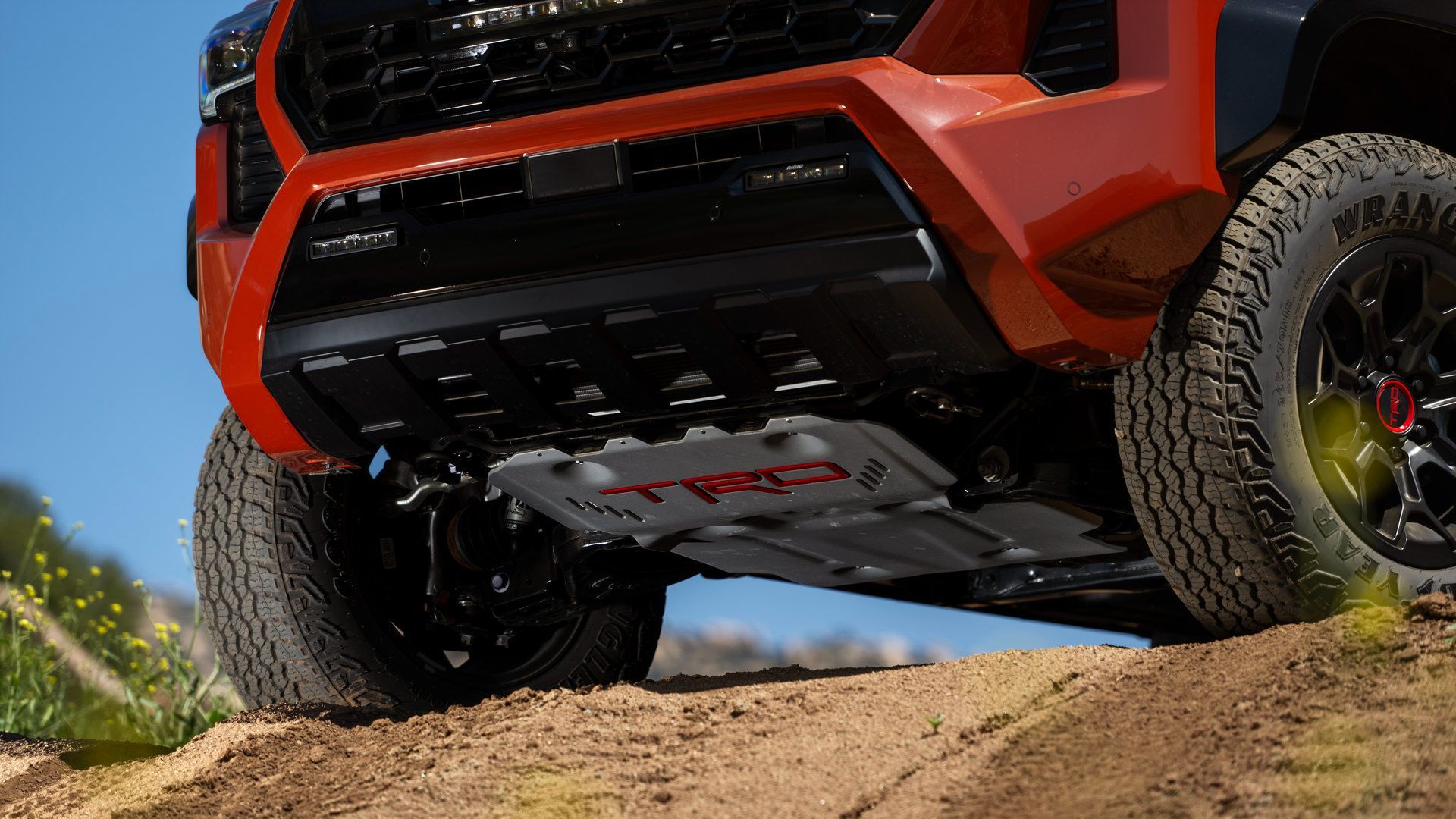 2027 Toyota Tacoma - low-angle close-up of a 2027 Toyota Tacoma TRD front skid plate and tire on a dirt trail - Orangeville Toyota - Toyota new car dealership in Orangeville, Ontario