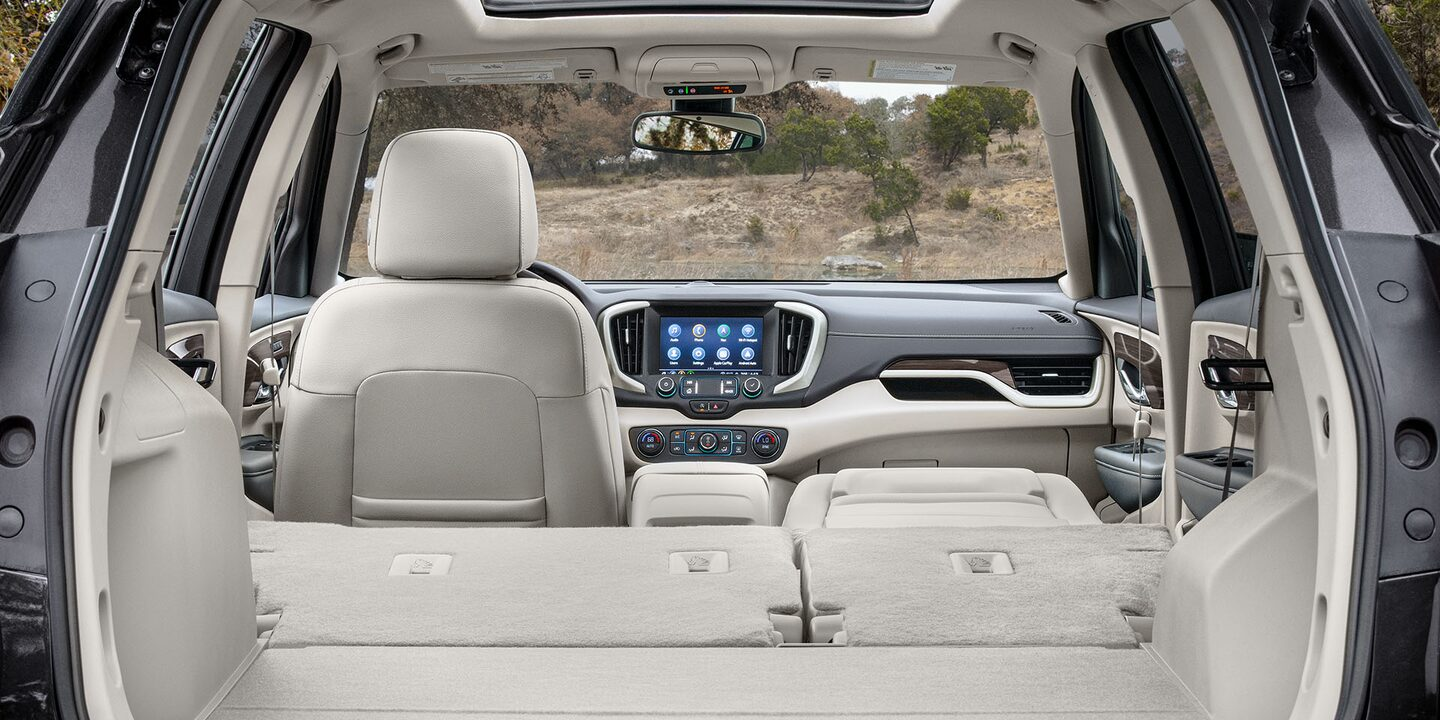 Interior view of a vehicle, showing the back of the front beige leather seat, with the dashboard and infotainment screen visible up front.