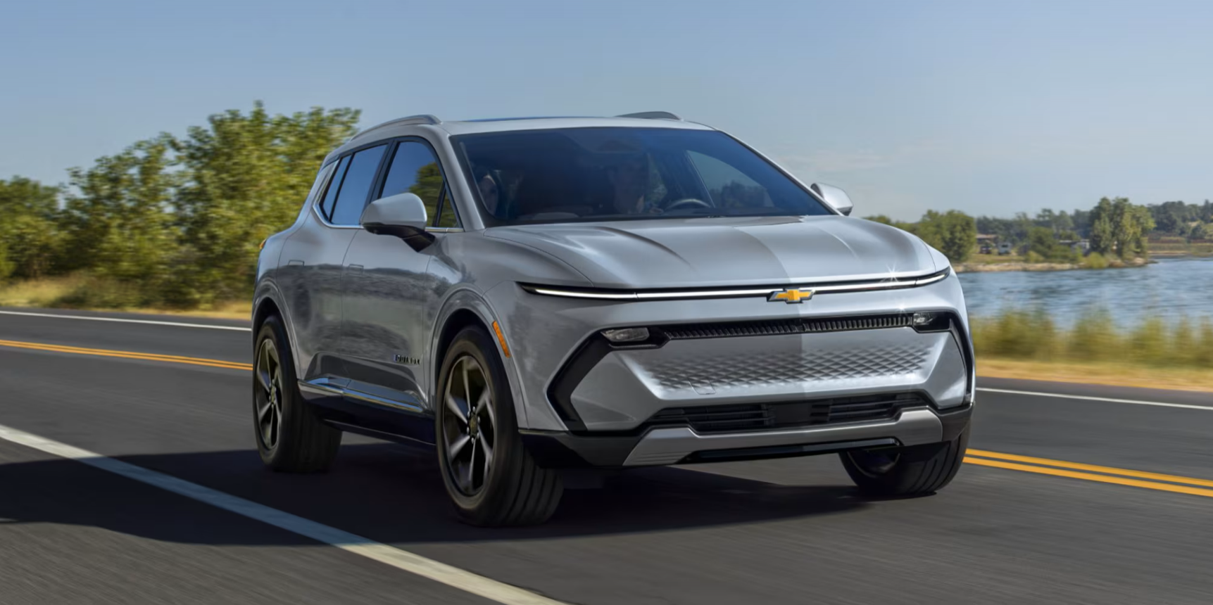 Grey 2025 Chevrolet Equinox EV driving on a road by a lake in Quebec.
