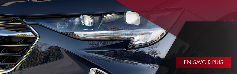 VUS Buick Envision 2022 vue de la calandre peinture bleue noire avec les phares avant allumés roulant sur la côte-nord