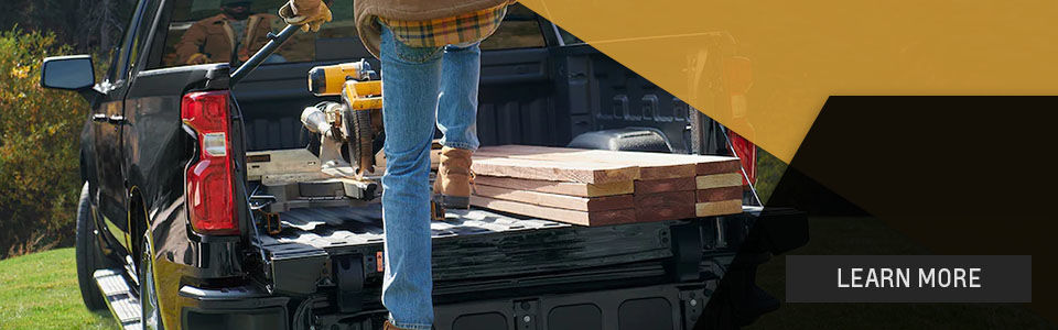 Learn more: Image of a chevrolet silverado 1500 pick-up seen from behind and a man cutting wood on the pick-up 