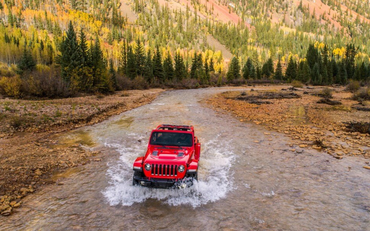 Bird's eye view of a 2023 Jeep Wrangler crossing a stream in the mountains