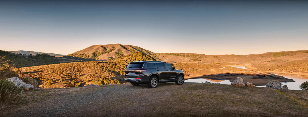 vue latérale arrière d'un Jeep Grand Cherokee 2022 sur une colline à l'aube