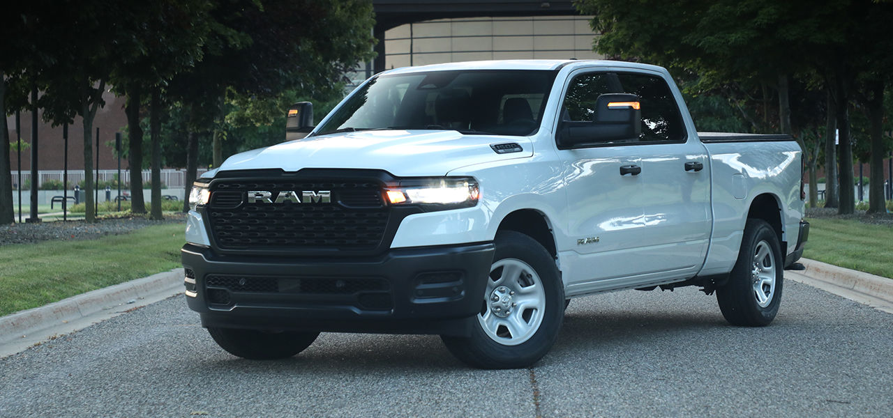 3/4 front and side view of RAM 1500 2025 stopped in a public yard with headlights on