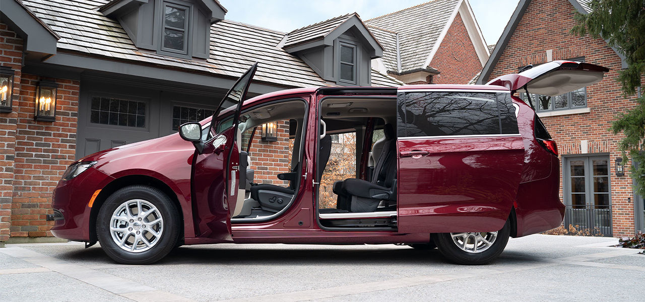 Side view of the Chrysler Grand Caravan 2024, parked in front of a house with the doors open.