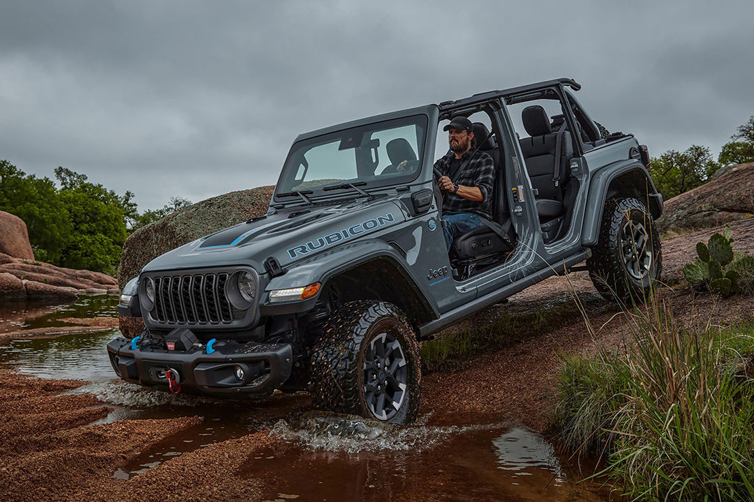 Front 3/4 front and side view of Jeep Wrangler hybrid 4xe 2024 on steep road, crossing a pool of water