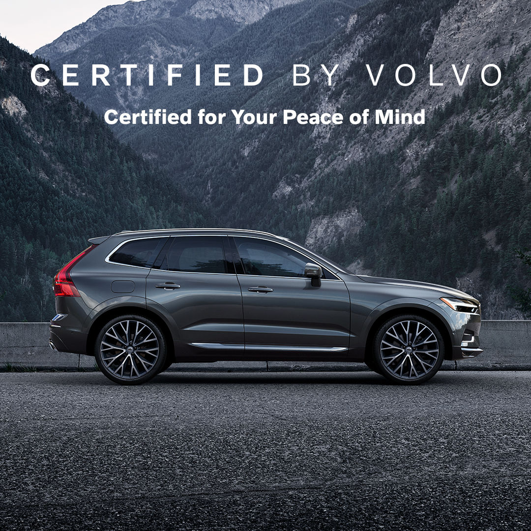 A side profile of a certified pre-owned dark grey Volvo XC60 in Kelowna is parked with the mountains behind it.