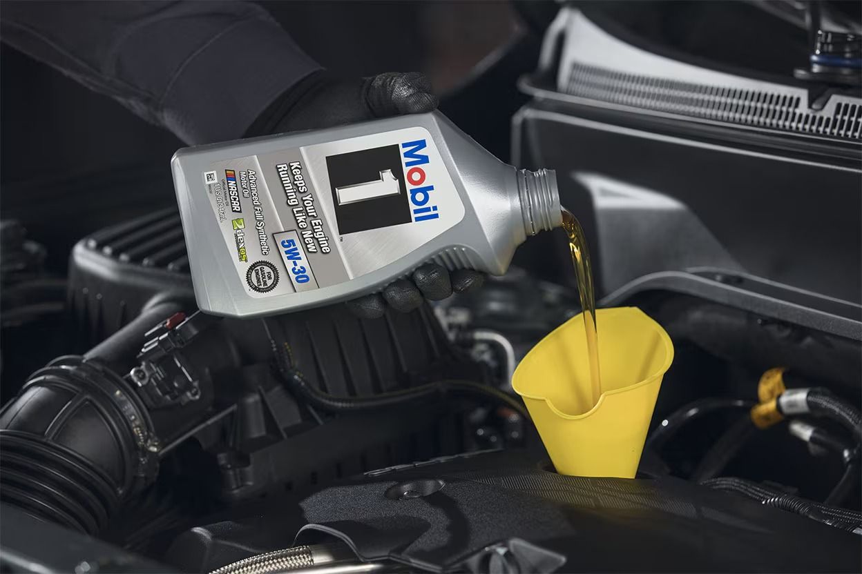 Mobil 1 engine oil being poured into a Chevrolet engine during dealership service.