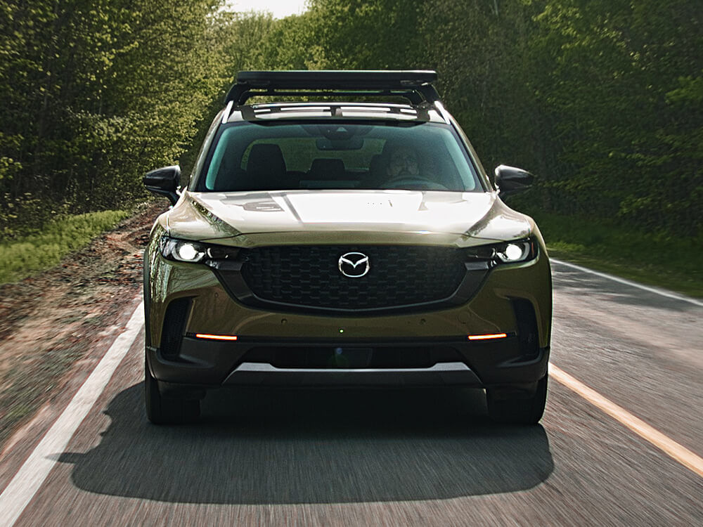 Un CX-50 sable de zircon métallisé circulant dans la forêt, sa calandre face à la caméra.