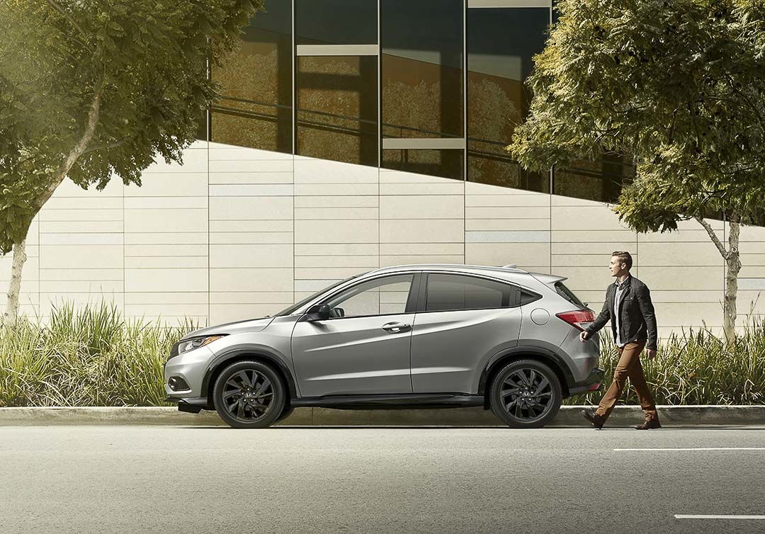 Side view of the 2021 Honda HR-V SUV parked at the edge of a sidewalk as the owner walks to drive the vehicle