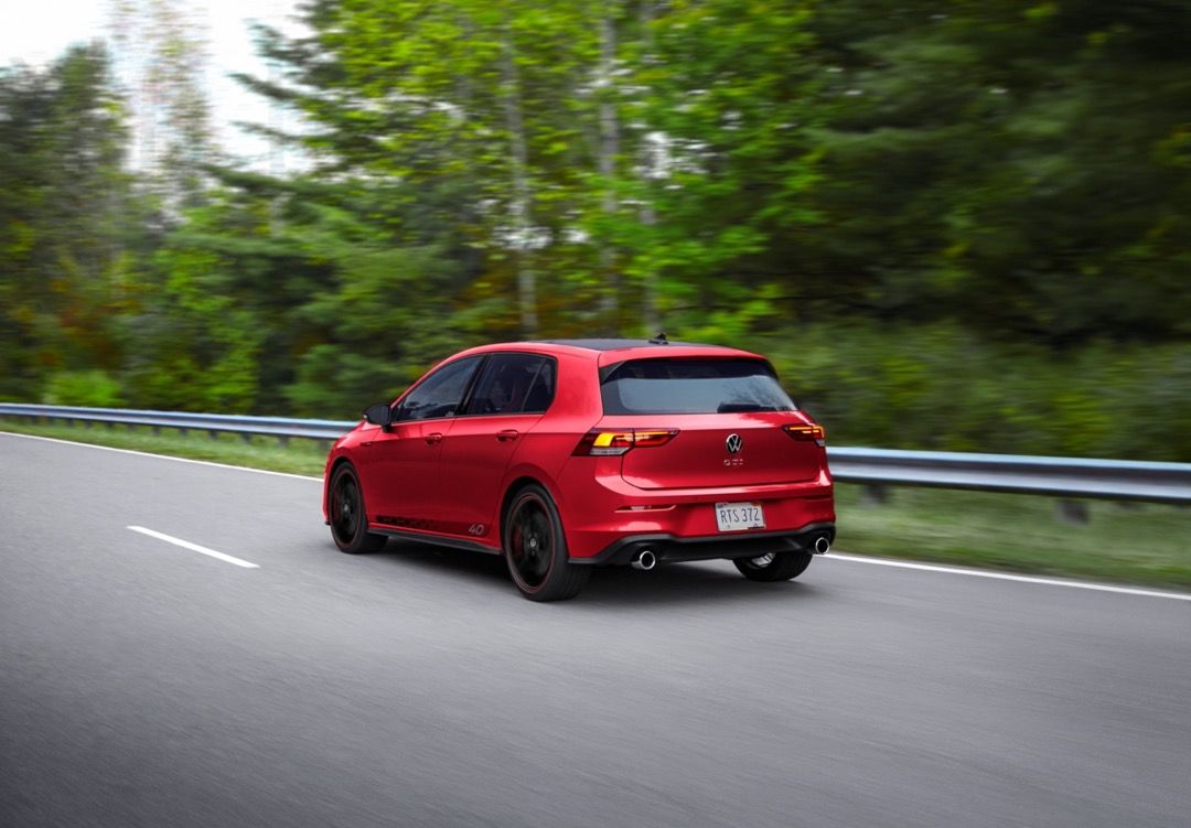 Rear 3/4 view of 2023 Volkswagen Golf GTI fuel efficient car driving on a road.