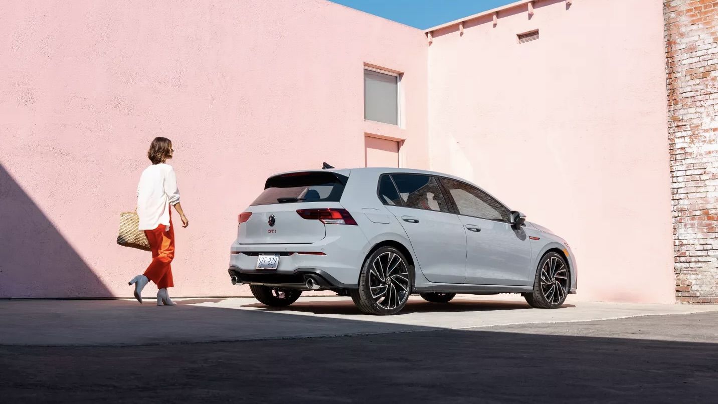 Vue 3/4 arrière de la Volkswagen Golf GTI 2024 et d'une femme qui s'apprête à monter à bord.