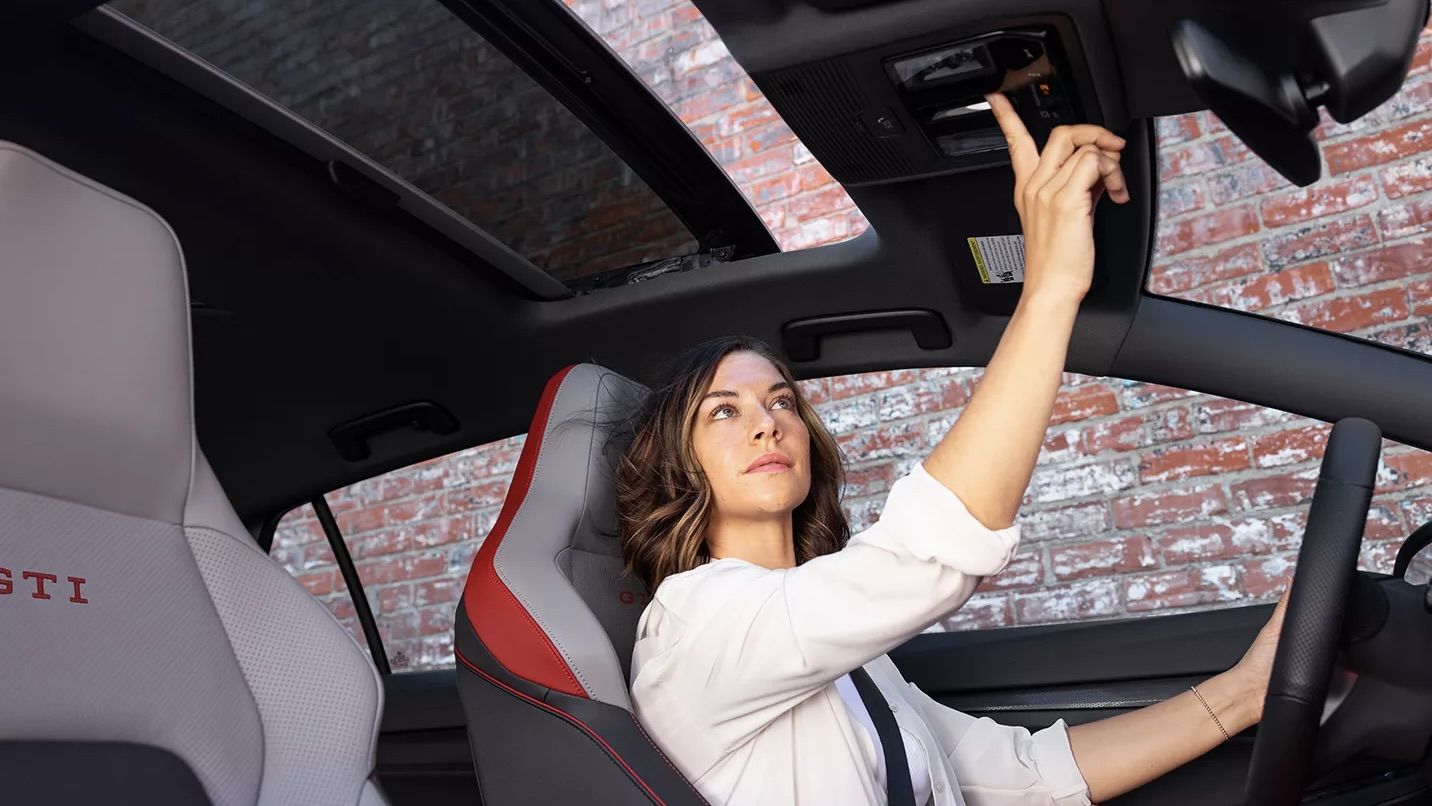 Nice view of the front seats and a woman opening the sunroof of her Volkswagen Golf GTI 2024.