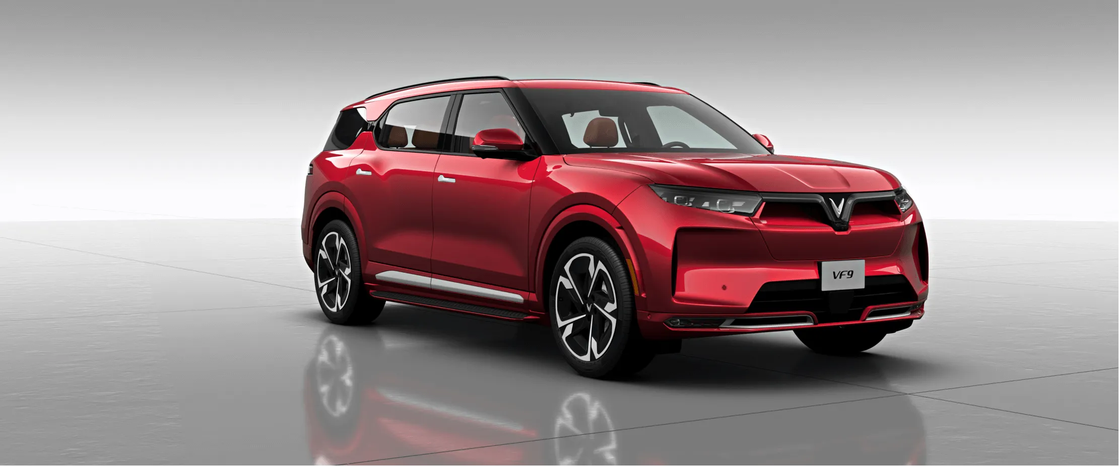 VinFast VF9 rouge en studio, illustrant une nouvelle marque de voiture &eacute;lectrique pr&eacute;sente dans le march&eacute; des VUS &eacute;lectriques.