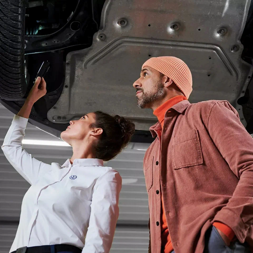 Conseillère Volkswagen montrant le dessous d’un véhicule pour l’inspection des freins et des filtres.