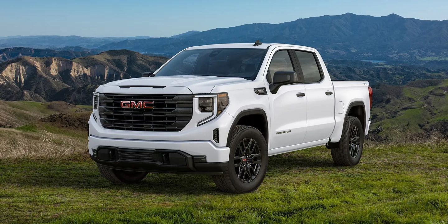 GMC Sierra 1500 2026 blanc garé sur un plateau verdoyant avec montagnes à l’arrière, démontrant son élégance et sa polyvalence.