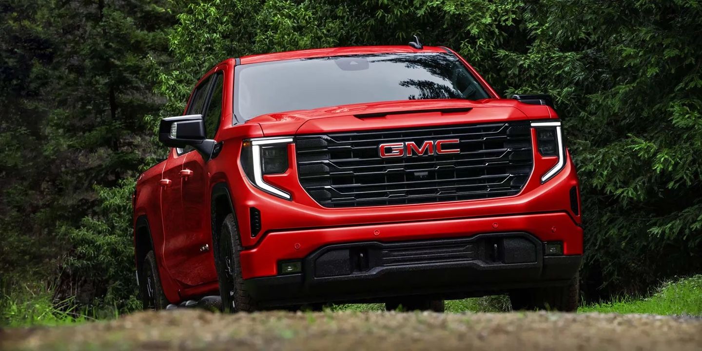 Vue avant du GMC Sierra 1500 2026 rouge dans une forêt dense, soulignant sa grille imposante et son design musclé.