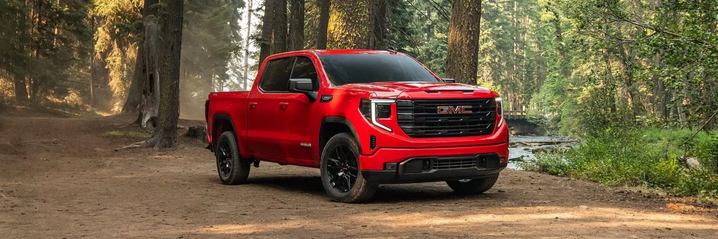 GMC Sierra 1500 2026 rouge stationné dans une clairière boisée, démontrant son allure robuste et son design haut de gamme.