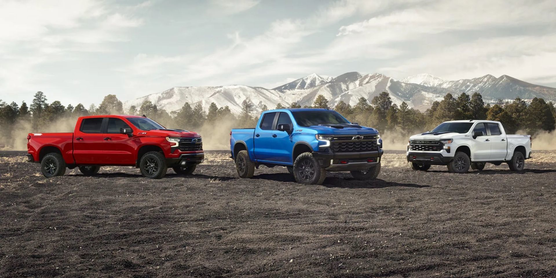 Trois Chevrolet Silverado 1500 2026 — rouge, bleu et blanc — stationnés en montagne sur sol volcanique, illustrant la gamme complète du modèle.