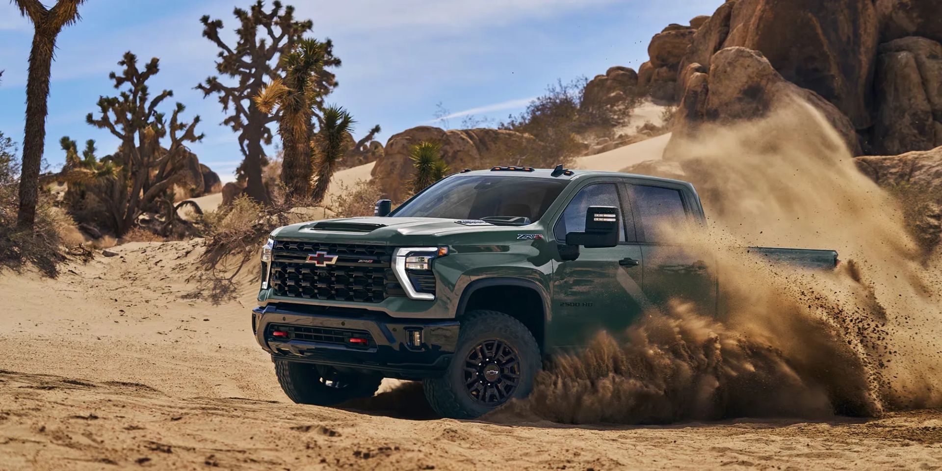 Chevrolet Silverado HD 2026 vert olive soulevant un nuage de sable dans le désert, illustrant sa puissance et ses capacités hors route.